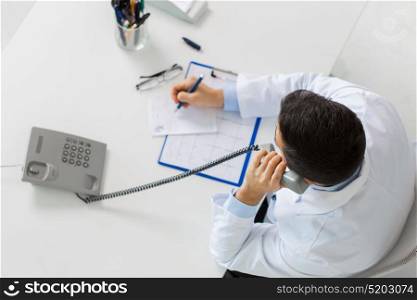 medicine, healthcare and people concept - doctor with cardiogram and prescription calling on phone at table in clinic. doctor with prescription calling on phone