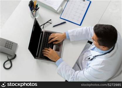 medicine, healthcare and people concept - doctor with cardiogram on clipboard typing on laptop computer sitting at table in clinic. doctor with cardiogram and laptop at clinic