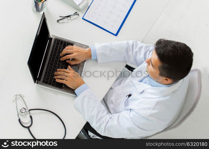 medicine, healthcare and people concept - doctor with cardiogram on clipboard typing on laptop computer sitting at table in clinic. doctor with cardiogram and laptop at clinic