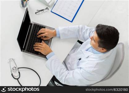medicine, healthcare and people concept - doctor with cardiogram on clipboard typing on laptop computer sitting at table in clinic. doctor with cardiogram and laptop at clinic
