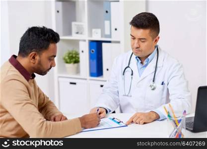 medicine, healthcare and people concept - doctor with clipboard and young male patient signing medical document at hospital. doctor and patient signing document at clinic