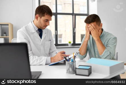 medicine, healthcare and people concept - doctor with clipboard talking to devastated male patient at medical office in hospital. doctor with clipboard and male patient at hospital