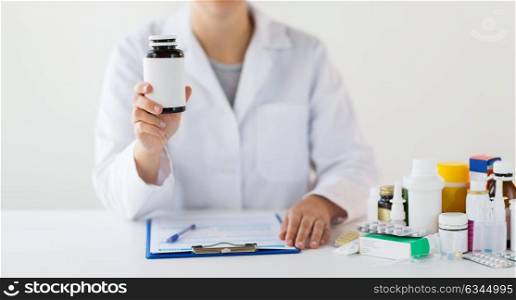 medicine, healthcare and people concept - doctor with drugs and clipboard showing jar with medication. close up of doctor with medicines and clipboard
