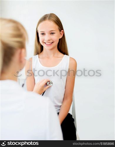 medicine, healthcare and people concept - doctor with stethoscope listening to girl heart beat or breath at hospital. doctor with stethoscope and girl at hospital