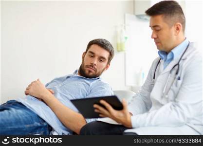 medicine, healthcare and people concept - doctor with tablet pc computer and young male patient having health problem meeting at hospital. doctor and man with health problem at hospital