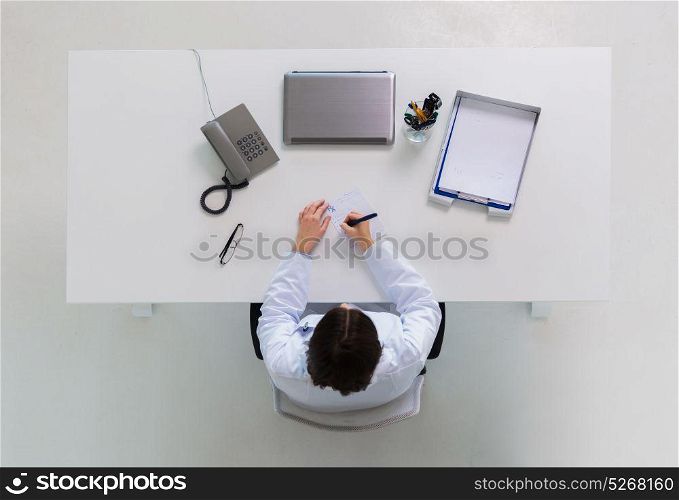 medicine, healthcare and people concept - doctor writing prescription at table. doctor writing prescription at table
