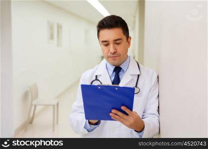 medicine, healthcare and people concept - doctor writing to clipboard at hospital