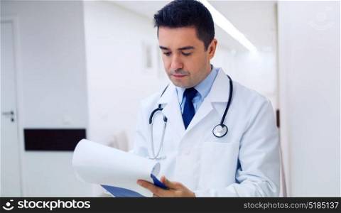 medicine, healthcare and people concept - doctor writing to clipboard at hospital. doctor writing to clipboard at hospital