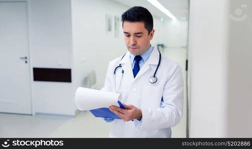 medicine, healthcare and people concept - doctor writing to clipboard at hospital. doctor writing to clipboard at hospital