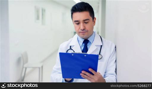 medicine, healthcare and people concept - doctor writing to clipboard at hospital. doctor writing to clipboard at hospital