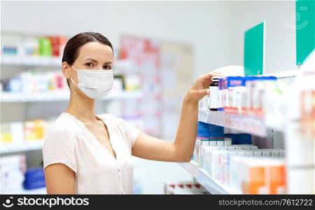 medicine, healthcare and people concept - female customer in face protective medical mask for protection from virus disease choosing drugs at pharmacy. female customer in mask choosing drugs at pharmacy