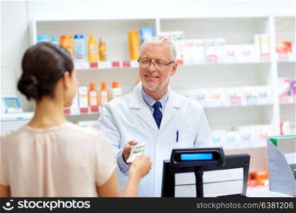 medicine, healthcare and people concept - female customer paying money to senior pharmacist at pharmacy cash register. customer giving money to pharmacist at drugstore