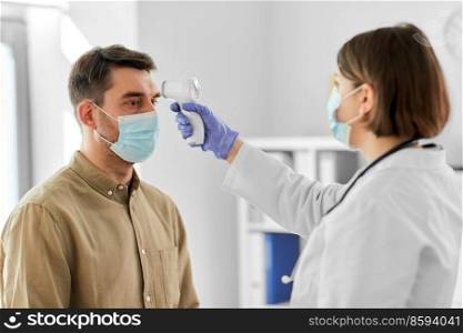 medicine, healthcare and people concept - female doctor in mask with infrared forehead thermometer measuring temperature of man patient at hospital. doctor with thermometer and man at hospital