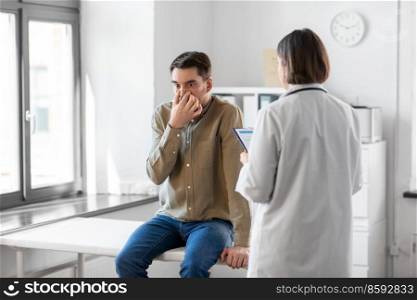 medicine, healthcare and people concept - female doctor with clipboard and man patient touching his nose at hospital. doctor and smiling man meeting at hospital