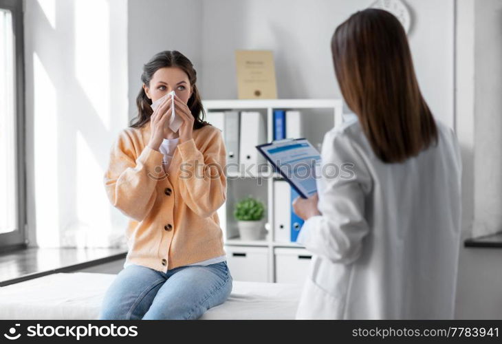 medicine, healthcare and people concept - female doctor with clipboard talking to woman patient blowing her nose with paper tissue at hospital. female doctor and woman blowing nose at hospital