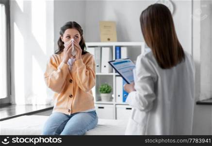medicine, healthcare and people concept - female doctor with clipboard talking to woman patient blowing her nose with paper tissue at hospital. female doctor and woman blowing nose at hospital