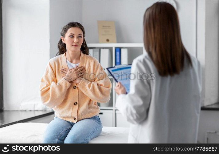 medicine, healthcare and people concept - female doctor with clipboard talking to woman holding to her chest patient at hospital. doctor with clipboard and woman at hospital