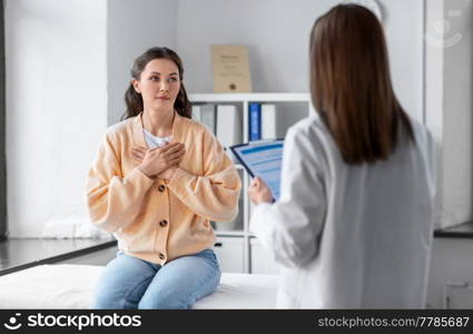 medicine, healthcare and people concept - female doctor with clipboard talking to woman holding to her chest patient at hospital. doctor with clipboard and woman at hospital