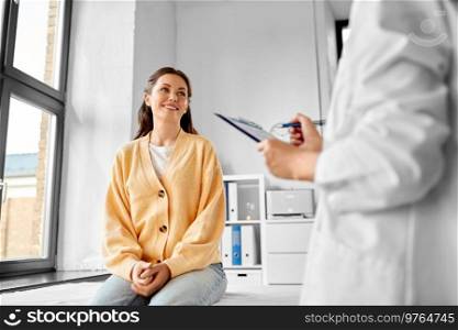 medicine, healthcare and people concept - female doctor with clipboard talking to smiling woman patient at hospital. doctor with clipboard and woman at hospital