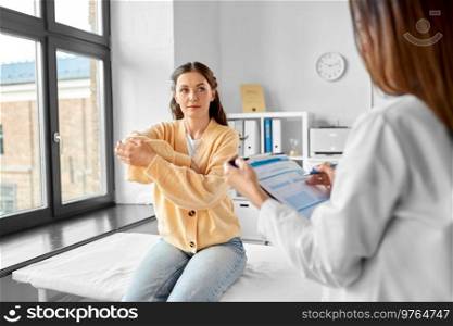 medicine, healthcare and people concept - female doctor with clipboard talking to woman showing her sore arm patient at hospital. female doctor and woman with sore arm at hospital