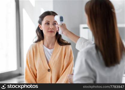 medicine, healthcare and people concept - female doctor with infrared forehead thermometer measuring temperature of woman patient at hospital. doctor with thermometer and woman at hospital