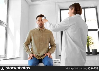 medicine, healthcare and people concept - female doctor with infrared forehead thermometer measuring temperature of man patient at hospital. doctor with thermometer and man at hospital