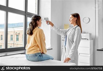 medicine, healthcare and people concept - female doctor with infrared forehead thermometer measuring temperature of woman patient at hospital. doctor with thermometer and woman at hospital