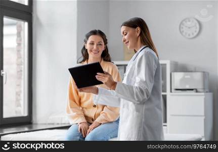 medicine, healthcare and people concept - female doctor with tablet pc computer talking to smiling woman patient at hospital. female doctor with tablet pc and woman at hospital