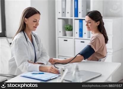 medicine, healthcare and people concept - female doctor with tonometer measuring woman patient’s blood pressure at hospital. female doctor with tonometer and patient at clinic