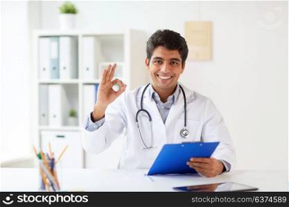 medicine, healthcare and people concept - happy male doctor with stethoscope and clipboard at clinic showing ok hand sign. happy doctor with clipboard at clinic showing ok