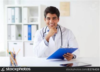 medicine, healthcare and people concept - happy male doctor with stethoscope and clipboard at clinic. happy doctor with clipboard at clinic