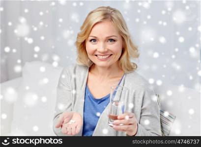 medicine, healthcare and people concept - happy middle aged woman with medication and water glass at home over snow