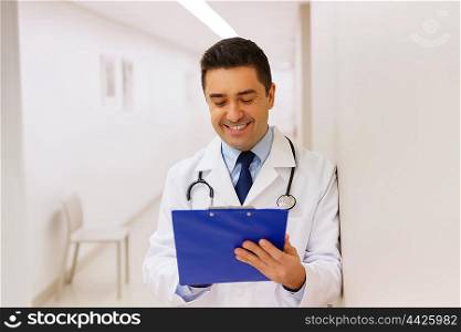 medicine, healthcare and people concept - happy smiling doctor writing to clipboard at hospital