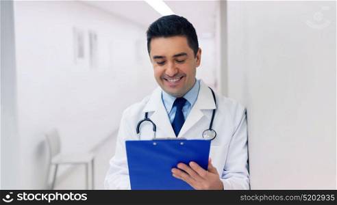 medicine, healthcare and people concept - happy smiling doctor writing to clipboard at hospital. happy doctor writing to clipboard at hospital