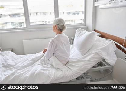 medicine, healthcare and people concept - lonely senior woman sitting in bed at hospital ward. lonely senior woman sitting in bed at hospital