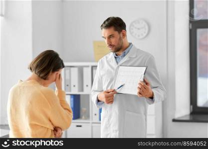 medicine, healthcare and people concept - male doctor or cardiologist with clipboard showing cardiogram to sad woman patient at hospital. doctor showing cardiogram to sad woman at hospital
