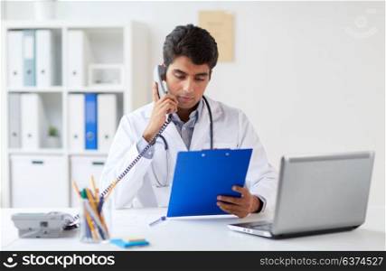 medicine, healthcare and people concept - male doctor with clipboard calling on phone at clinic. doctor with clipboard calling on phone at clinic