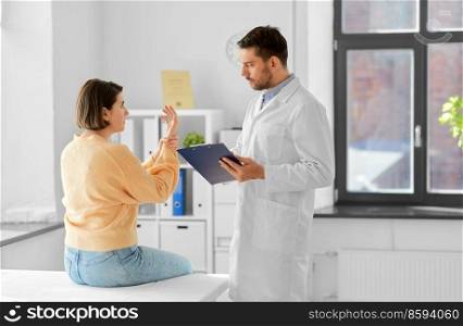 medicine, healthcare and people concept - male doctor with clipboard talking to woman showing her sore arm patient at hospital. male doctor and woman with sore arm at hospital