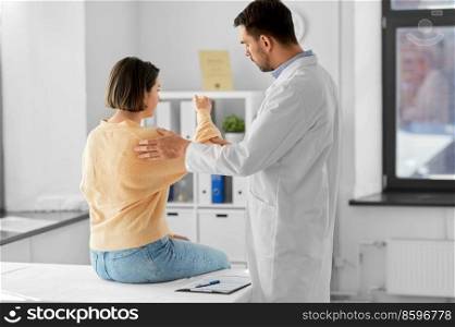 medicine, healthcare and people concept - male doctor with clipboard talking to woman showing her sore arm patient at hospital. male doctor and woman with sore arm at hospital