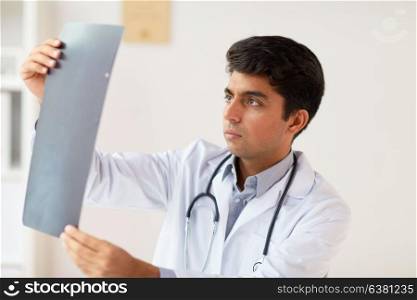 medicine, healthcare and people concept - male doctor with stethoscope looking spine at x-ray scan at clinic. doctor looking at spine x-ray scan at clinic
