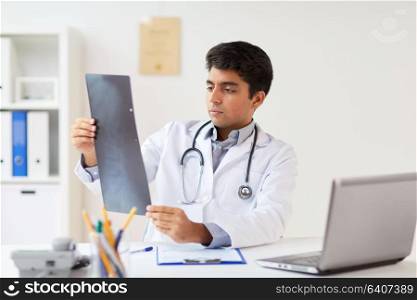 medicine, healthcare and people concept - male doctor with stethoscope looking spine at x-ray scan at clinic. doctor looking at spine x-ray scan at clinic