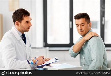 medicine, healthcare and people concept - male patient showing sore arm to doctor at medical office in hospital. patient showing sore shoulder to doctor at clinic