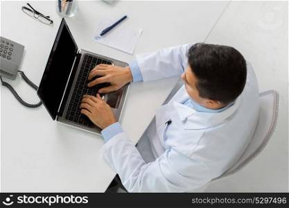 medicine, healthcare and people concept - man doctor with prescription typing laptop computer sitting at table in clinic. man doctor typing on laptop at clinic