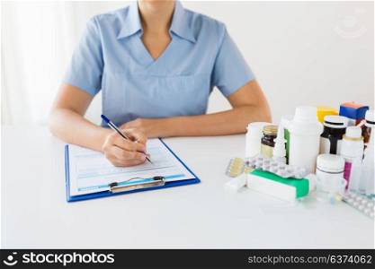 medicine, healthcare and people concept - nurse or doctor with drugs and clipboard writing prescription or medical report at hospital. doctor with medicines and clipboard at hospital