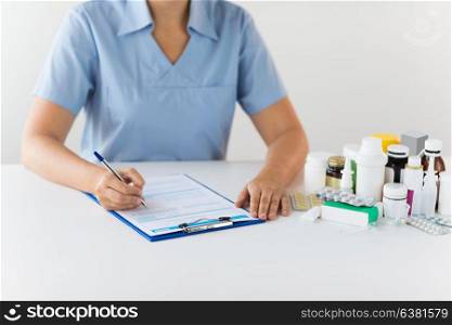 medicine, healthcare and people concept - nurse or doctor with drugs and clipboard writing prescription or medical report at hospital. doctor with medicines and clipboard at hospital