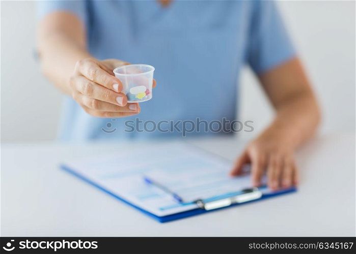 medicine, healthcare and people concept - nurse or doctor with pills in medical cup and clipboard. close up of doctor with pills in medical cup