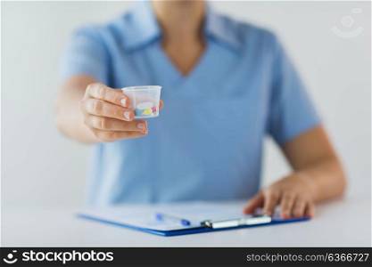 medicine, healthcare and people concept - nurse or doctor with pills in medical cup and clipboard. close up of doctor with pills in medical cup