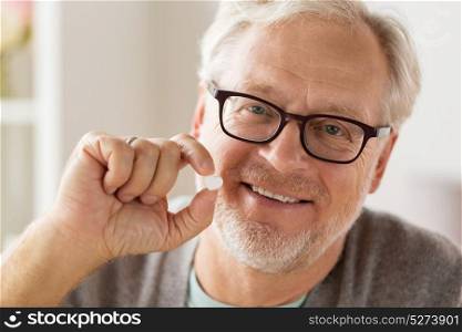 medicine, healthcare and people concept - portrait of happy smiling senior man with heart shaped pill. happy senior man with heart shaped pill