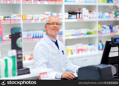 medicine, healthcare and people concept - senior apothecary at pharmacy cash register. senior apothecary at pharmacy cash register