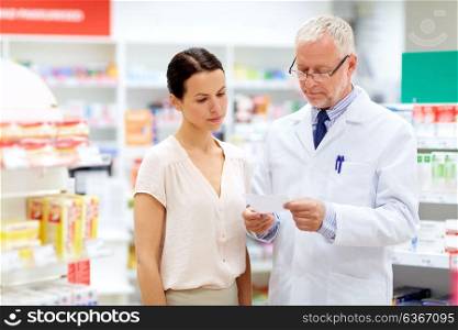 medicine, healthcare and people concept - senior apothecary reading prescription from female customer at pharmacy. apothecary and woman with prescription at pharmacy
